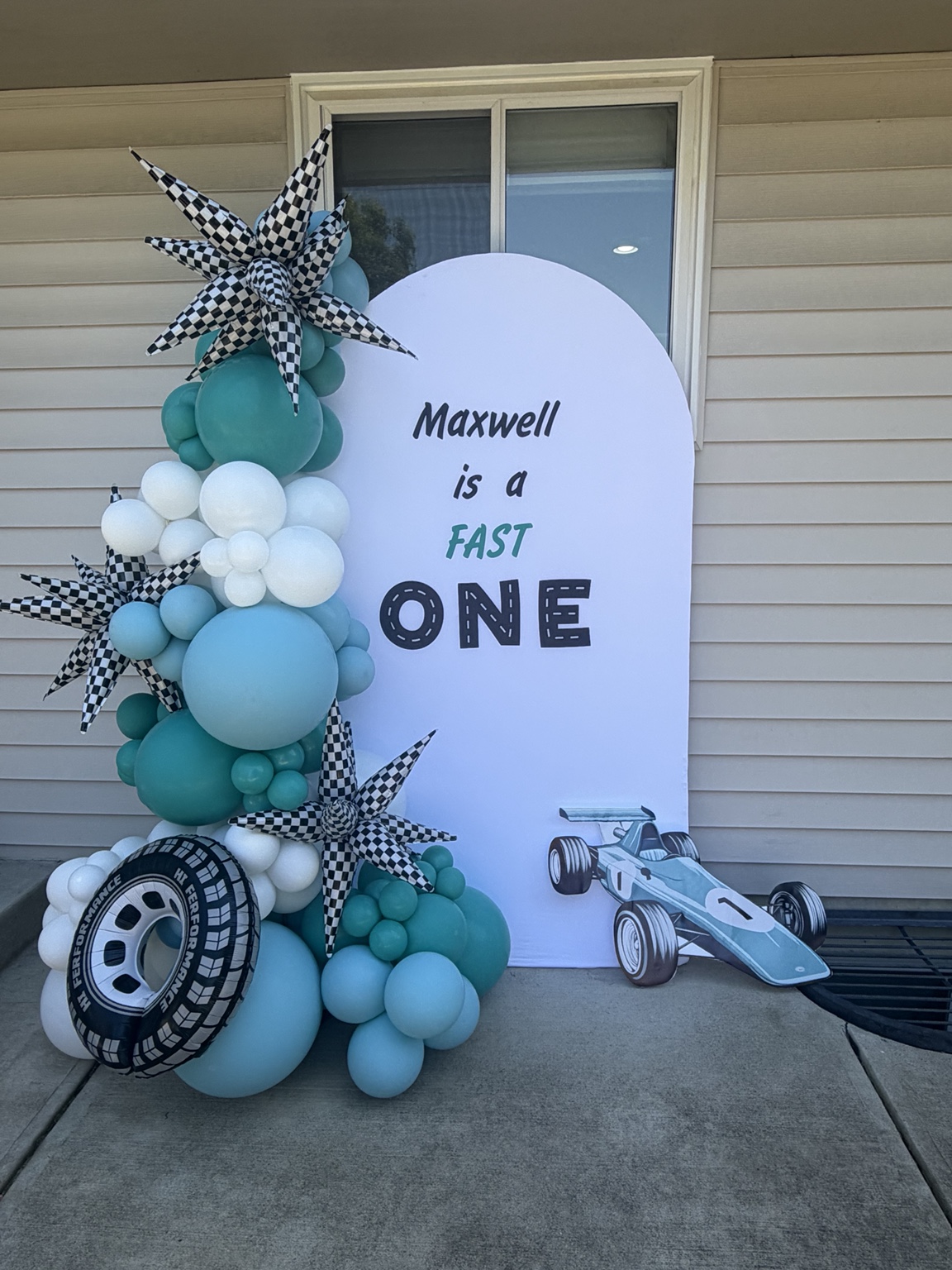Teal and blue birthday balloon backdrop with checkerboard stars and race car details