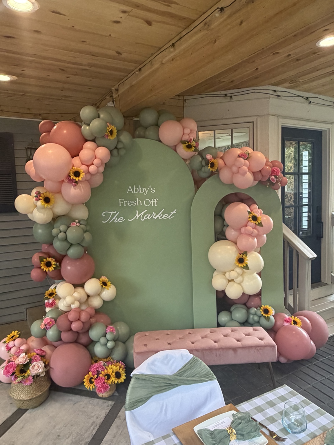 Sage and blush balloon installation with sunflowers and layered green arch backdrops