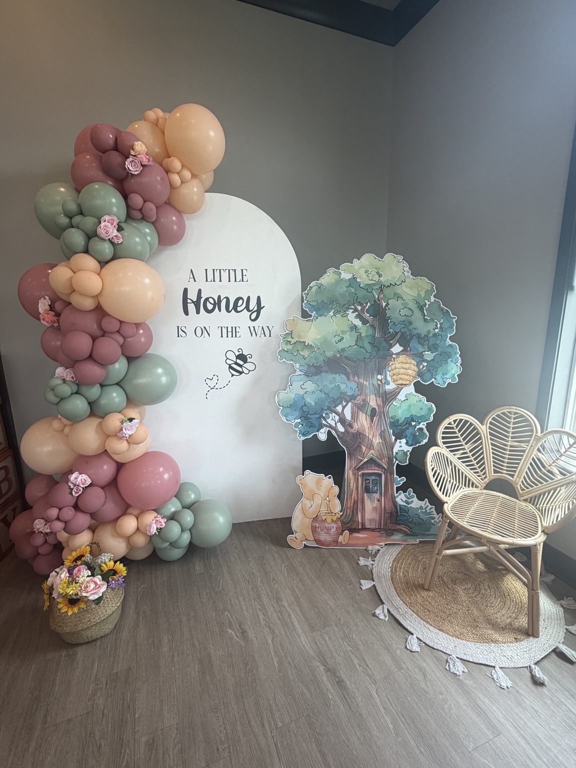 Mauve and pastel balloon arch with flowers, honeybee-themed backdrop and wicker chair