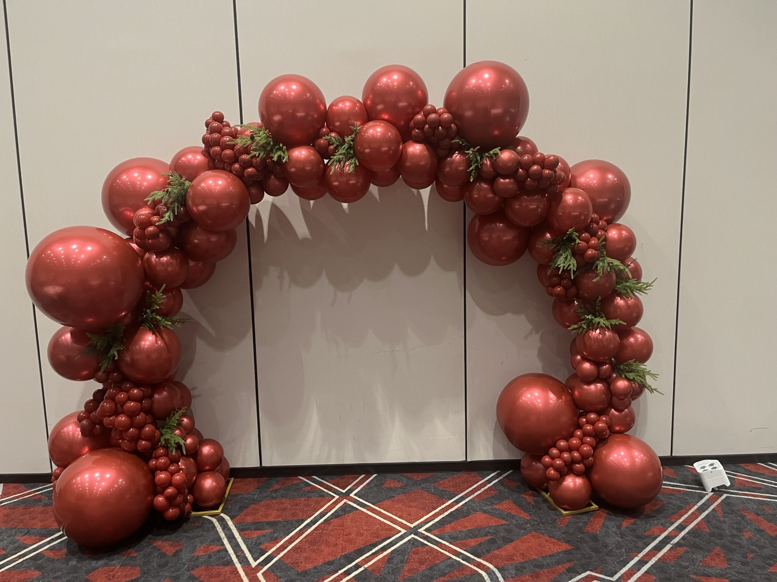 Dramatic monochromatic metallic red balloon arch with small sculptural clusters and evergreen accents