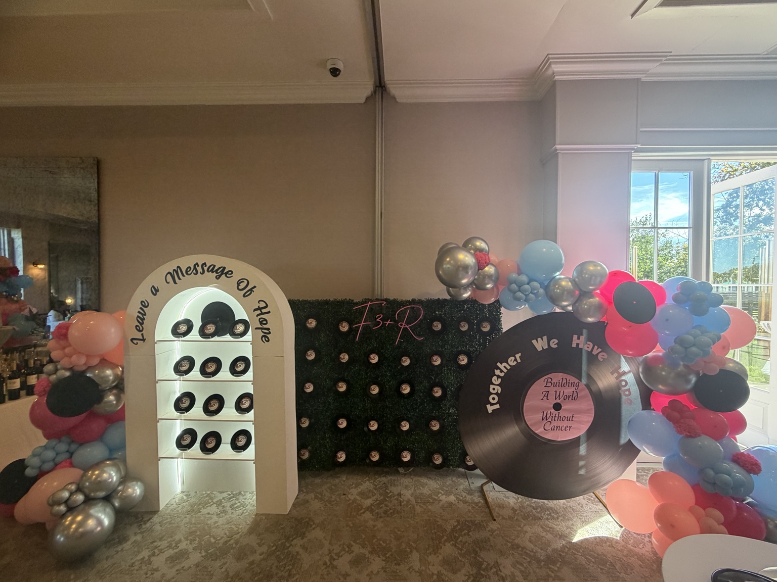 Pink, blue and silver balloon structures surrounding a custom charity-event vinyl record feature and message-of-hope display